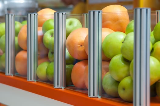 A large glass container showcase fresh fruit apples and oranges, focus is positioned on oranges
