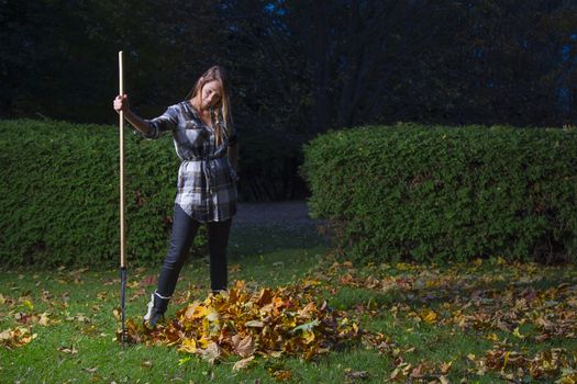 twenty something girl holding a rake and looking at a small pile of leaves