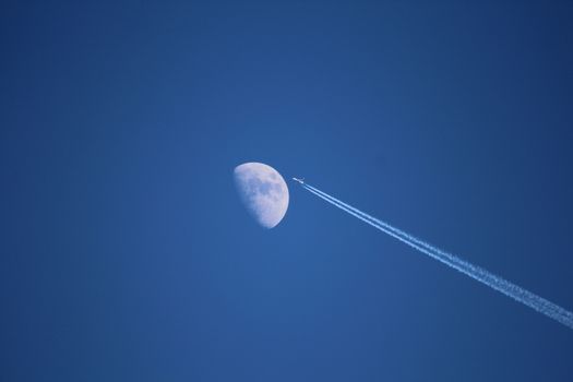 Jet airplane with trail of fuel on blue sky and big moon