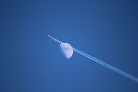 Jet airplane with trail of fuel on blue sky and big moon