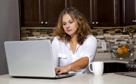 woman drinking coffee while working on ther laptop in the kitchen