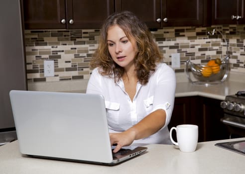 woman drinking coffee while working on ther laptop in the kitchen