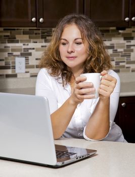 woman drinking coffee while working on ther laptop in the kitchen