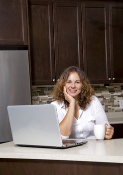 woman drinking coffee while working on the laptop in the kitchen