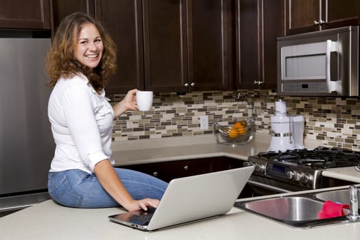 woman drinking coffee while working on the laptop in the kitchen