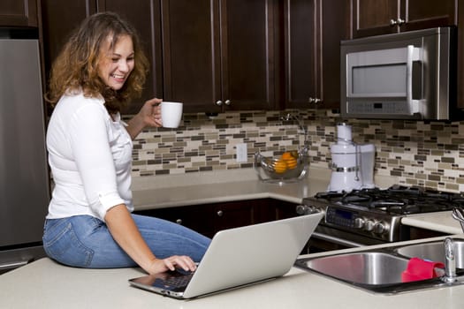 woman drinking coffee while working on the laptop in the kitchen