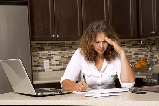 stressed woman looking at bills while sitting in the kitchen 