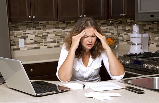 stressed woman looking at bills while sitting in the kitchen 