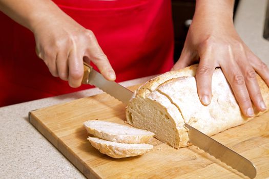caucasian woman cutting a bread with knife in kitchen