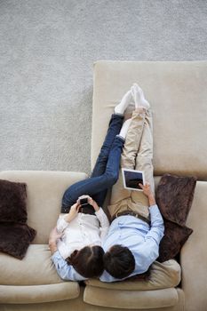 Couple using digital tablet at home sitting on sofa, top view