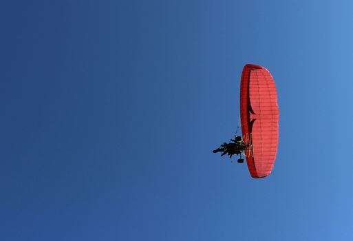 Paraglider and a passenger on a red paraglider with a motor are flying in the blue sky.