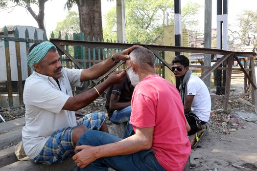 Street barber shaving a man using an open razor blade on a street in Kolkata, West Bengal, India