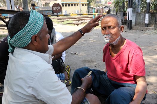 Street barber shaving a man using an open razor blade on a street in Kolkata, West Bengal, India
