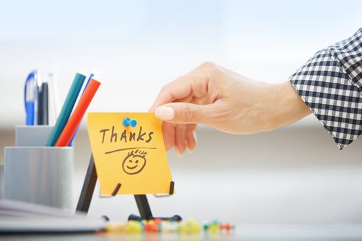 Human hand holding adhesive note with Thanks text