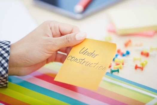 Human hand holding adhesive note with Under construction text