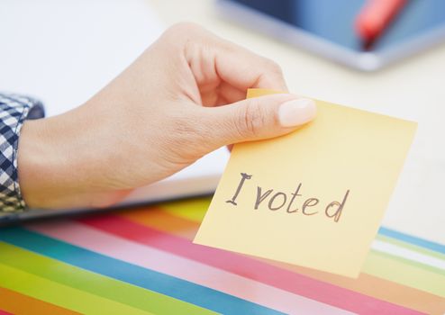Human hand holding adhesive note with I voted text
