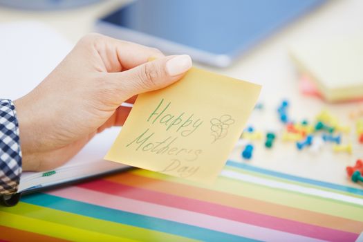 Human hand holding adhesive note with Happy mothers day text