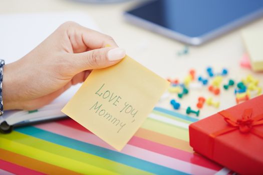 Human hand holding adhesive note with Love you mommy text