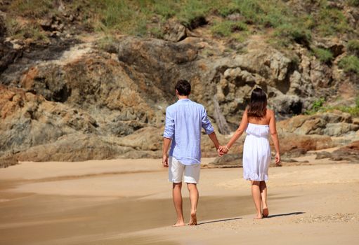 Cheerful couple walking on beach on rock background