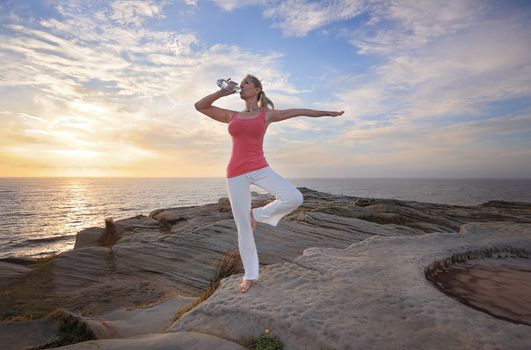 Woman drinking water during an exercise or fitness yoga routine by the ocean in the morning light