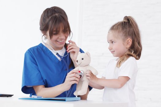 Young smiling female doctor and her little patient with teddy bear