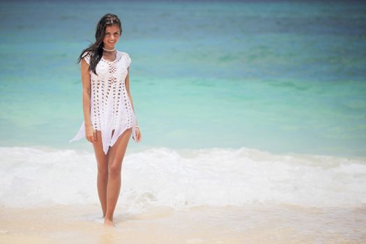 Beautiful young woman in dress on beach with hands raised
