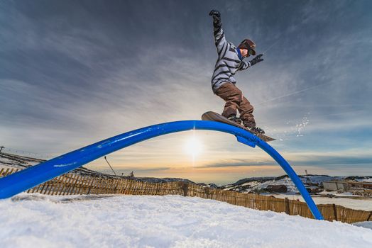 A snowboarder executes a radical slide on a rail in a snow park.