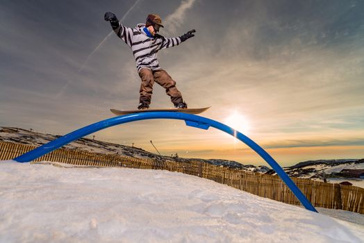 A snowboarder executes a radical slide on a rail in a snow park.