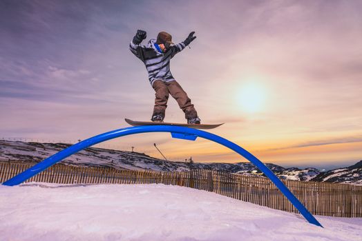 A snowboarder executes a radical slide on a rail in a snow park.