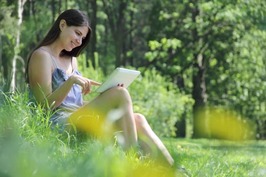 Young woman using tablet outdoor sitting under tree in park
