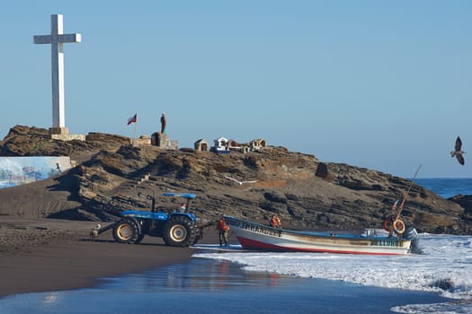 Tractor pulling a fishing boat clear of the sea on the sandy beach in the fishing village of Curanipe, Chile.