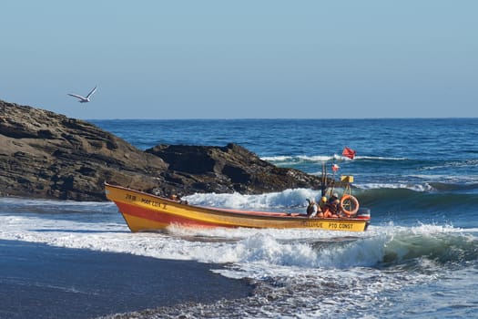 Fishing boat coming ashore on the sandy beach in the fishing village of Curanipe, Chile. Once the boats are beached on the sand, a tractor is used to pull the boats to safer ground.