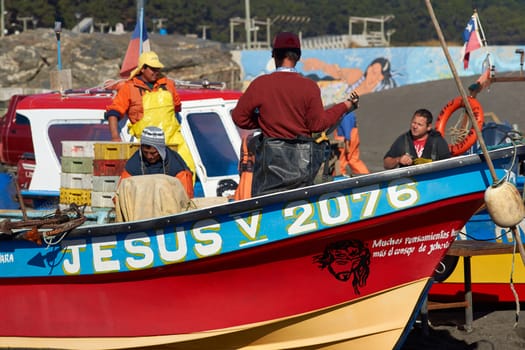 Fishermen removing merluza (pacific hake) from the fishing nets of boats that have recently been pulled out of the sea onto the sandy beach in the fishing village of Curanipe, Chile.