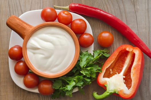 Ceramic dishes with sour cream, and ingredients for salad on an old wooden table.