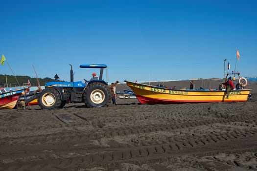 Tractor pulling a fishing boat clear of the sea on the sandy beach in the fishing village of Curanipe, Chile.