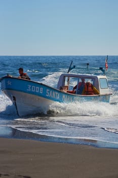 Fishing boat coming ashore on the sandy beach in the fishing village of Curanipe, Chile. Once the boats are beached on the sand, a tractor is used to pull the boats to safer ground.