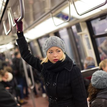 Beautiful blonde caucasian lady wearing winter coat traveling by metro in rush hour. Public transport.