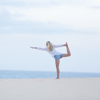Relaxed woman enjoying enjoying peace and freedom during her morning walk on vacations, streching in yoga like pose at beach.