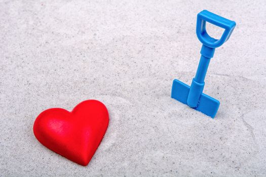 Red heart and blue scoop on a grey sand background