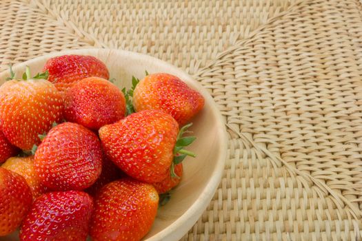 fresh strawberry in wooden bowl on wickerwork background