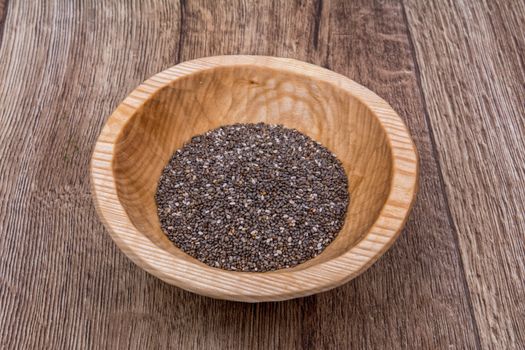 Chia seeds in a wooden bowl on a brown wooden background