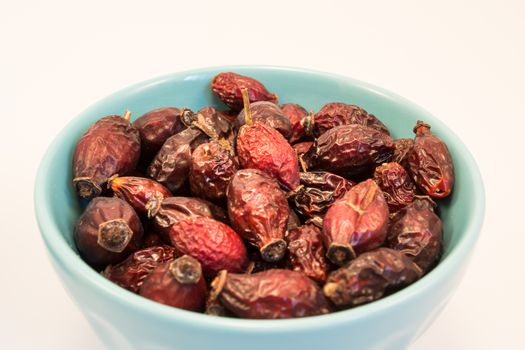 Dry rosehips in bowl on white background