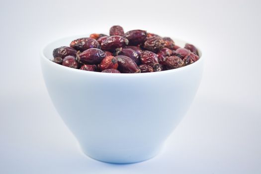 Bowl of dry rosehips in white bowl on white background