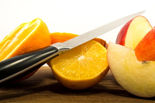 Orange, lemon and apple with knife on wooden plate