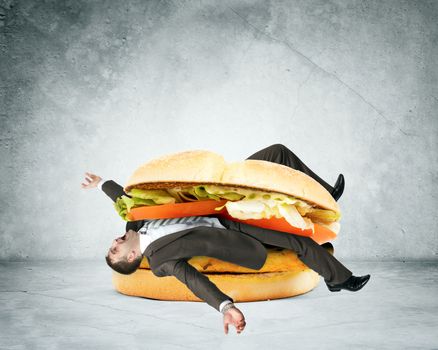 Businessman inside hamburger on grey wall background