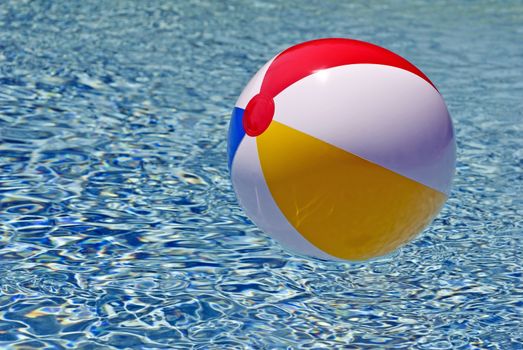 Horizontal shot of a brightly colored beach ball floating in blue waters in swimming pool