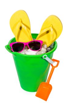 Vertical isolated shot of brightly colored green pail with shovel, yellow flip flops and sunglasses