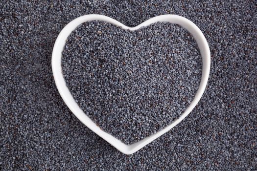 Poppy seed background. Poppy seeds in heart shaped bowl, top view. Healthy eating. 