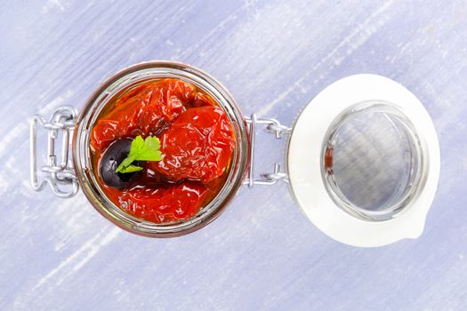Dry tomatoes in oil in jar on blue wooden background. Culinary eating. 