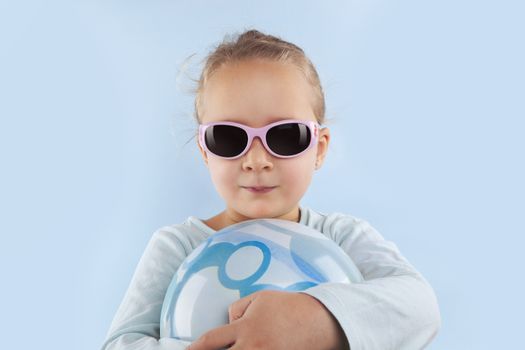 Summer. Adorable beautiful girl with ball and sunglasses against blue background. Summer background.